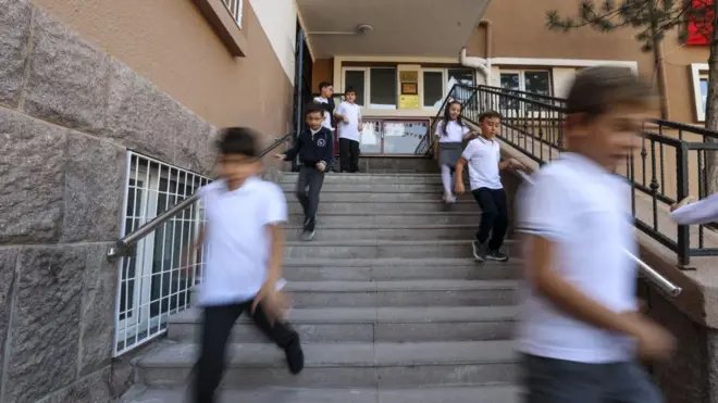 Bir okul merdiveninden aşağıda doğru koşan çocuklar.