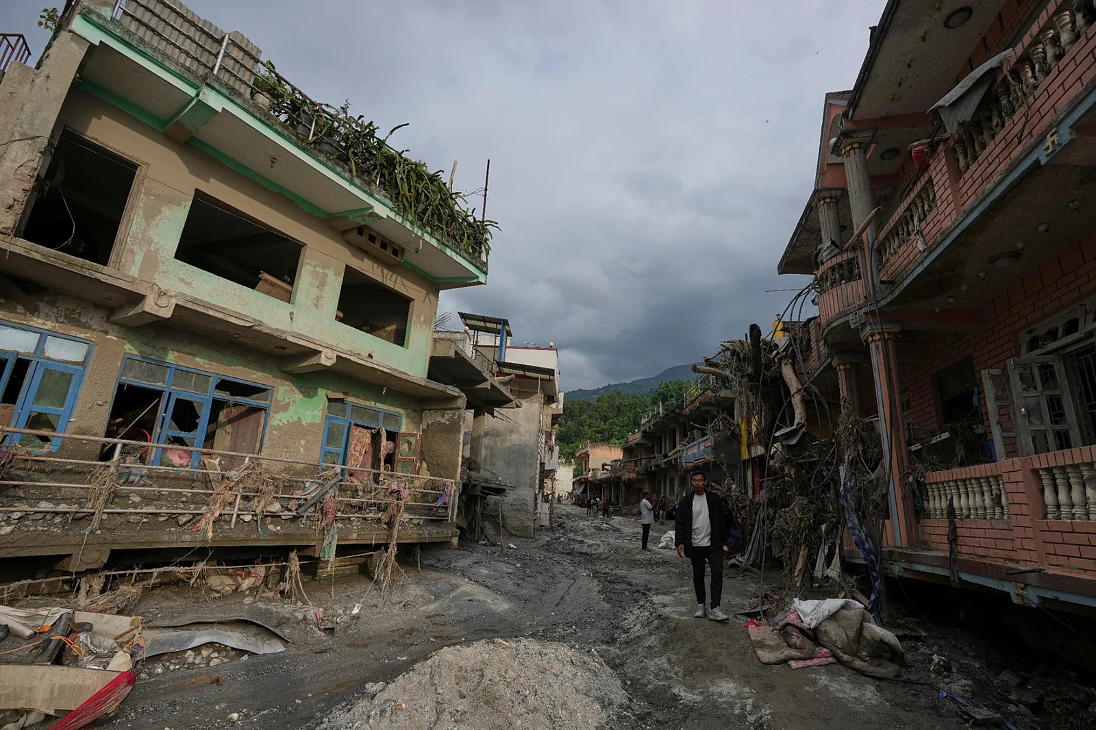 Nepal'in Nuwakot bölgesindeki Devighat çevresinde ani selin ardından, hasar görmüş binaların sıralandığı bir caddede yürüyen insanlar, 28 Ağustos 2026