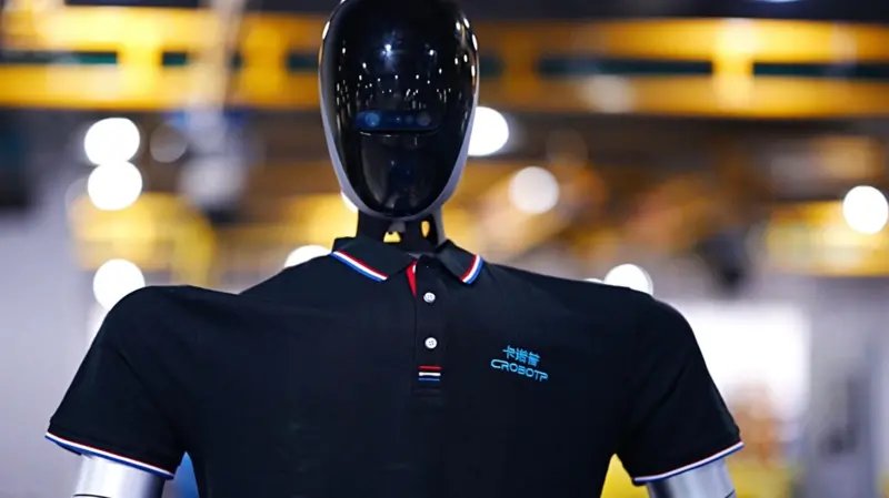 Fabrikada çalışan, siyah polo tişört giyen bir robot.