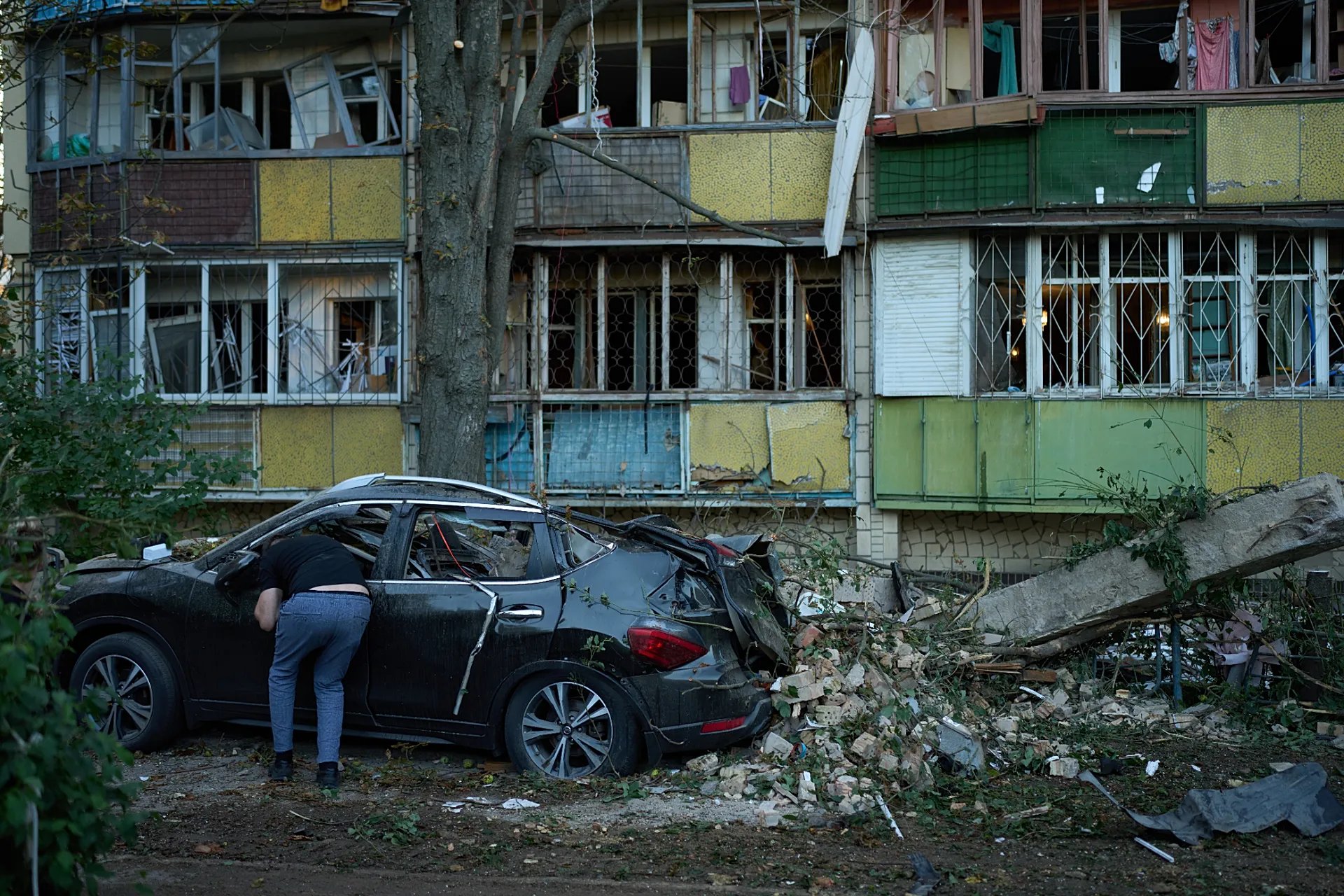 Kiev'de bir kişi, Rus saldırısının ardından ağır hasar gören konut binalarının yanında duran hurdaya dönmüş bir otomobilin içine bakıyor, 20 Ağustos 2026.