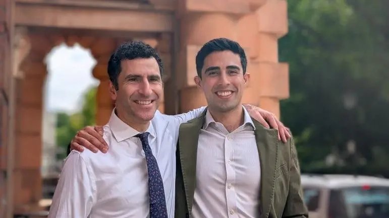 Profesör Hani Marcus ve Bay Danyal Khan'ın dışarıda dururken çekilmiş fotoğrafı. İkisinin de koyu kahverengi saçları var. Biri beyaz gömlek ve mavi-beyaz kravat takmış. Diğeri açık renkli bir gömlek ve haki renkli bir ceket giymiş.