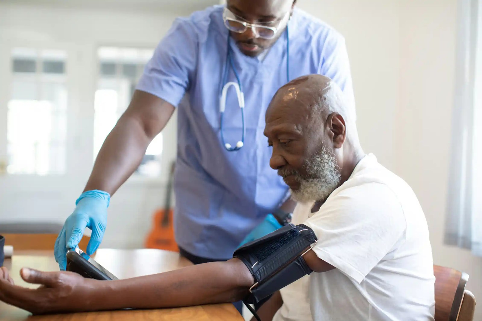 A man in blue scrubs taking the blood pressure of a seated older man