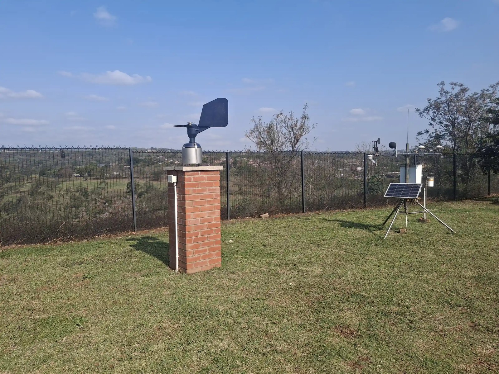 A small brick tower with a metal contraption on top with a kind of wing sticking out