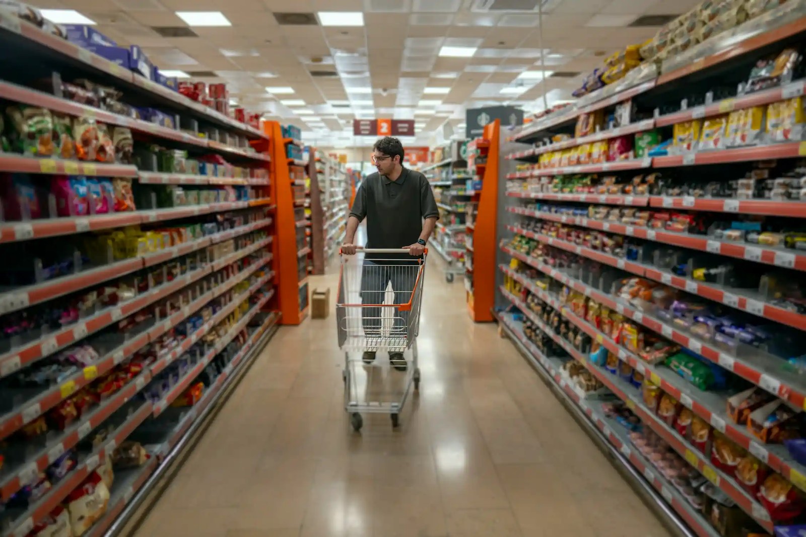 A man walks towards us, pushing a trolley down a supermarket aisle