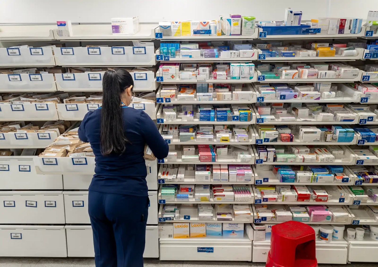 A pharmacist in front of shelves of medications.