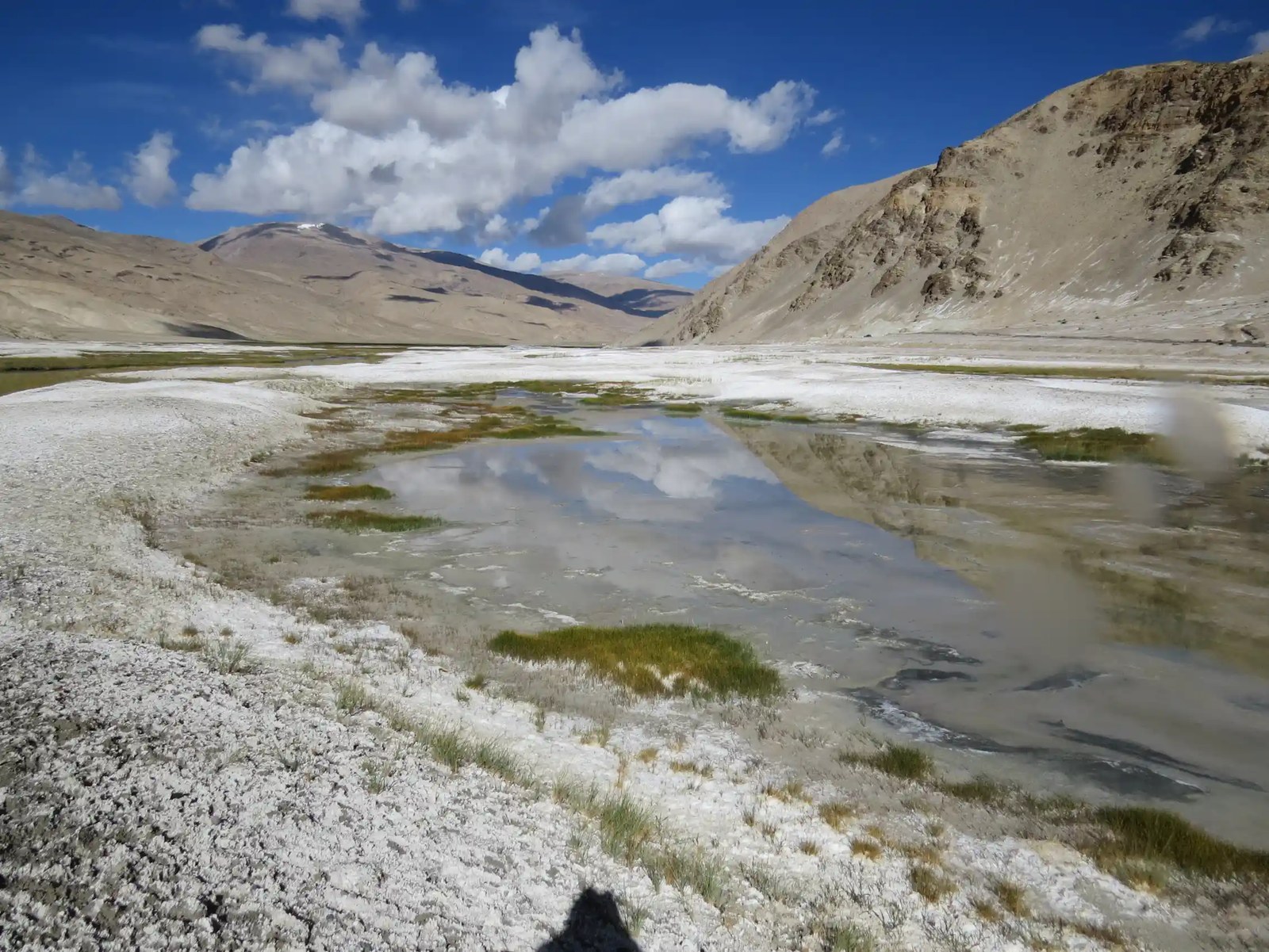 A pond among mountains surrounded by white crystals on the ground.