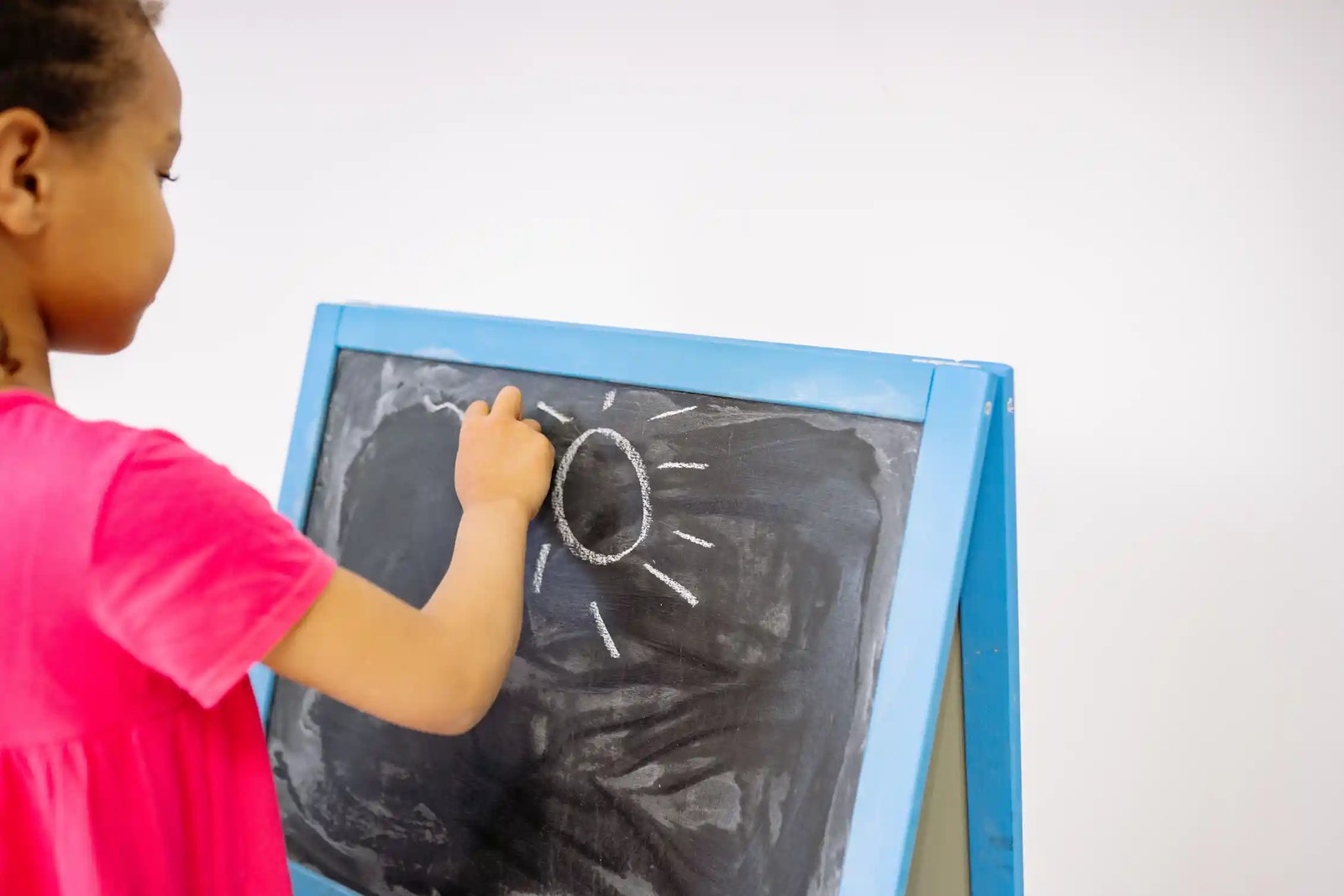 A child at a chalkboard drawing a sun.