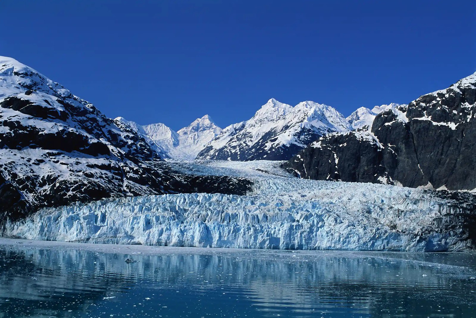 landscape shot of a glacier ending in calm water, mountains around.