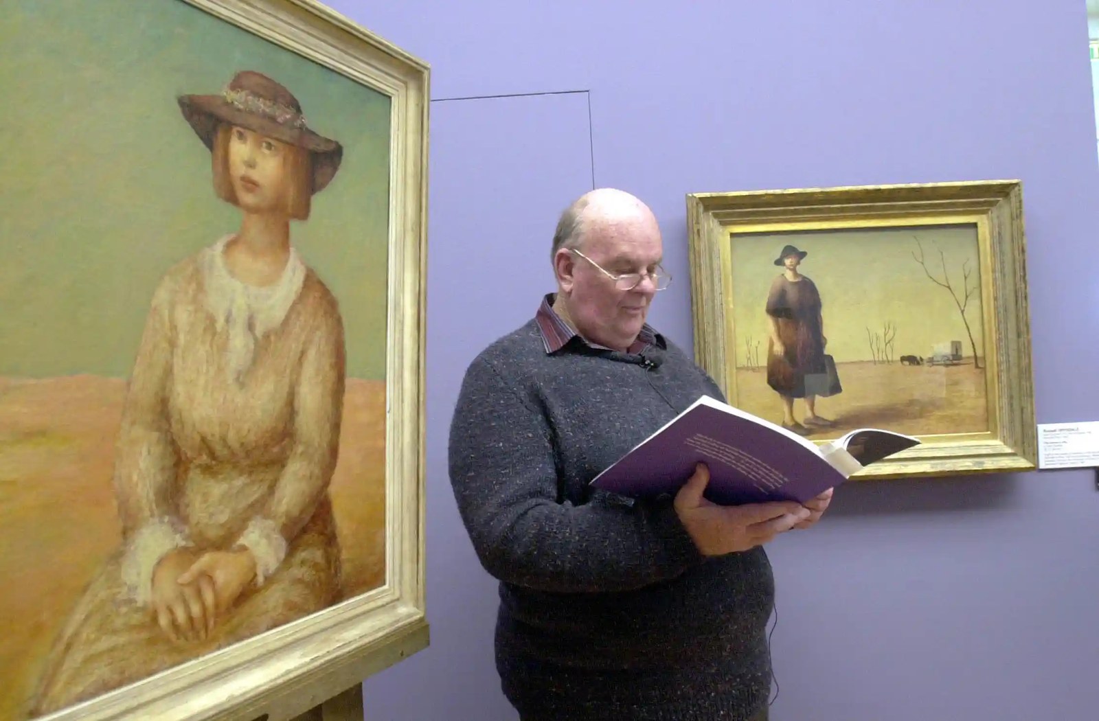 Les Murray standing between two paintings by Russell Drysdale and reading from a large book