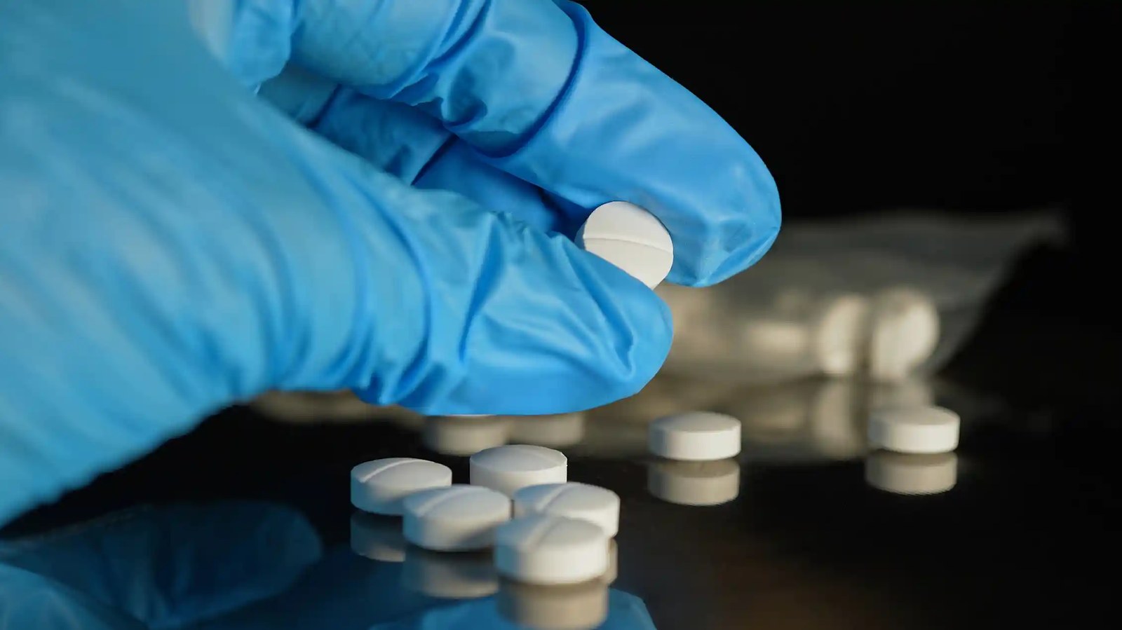 Hand in blue glove studying a white pill.