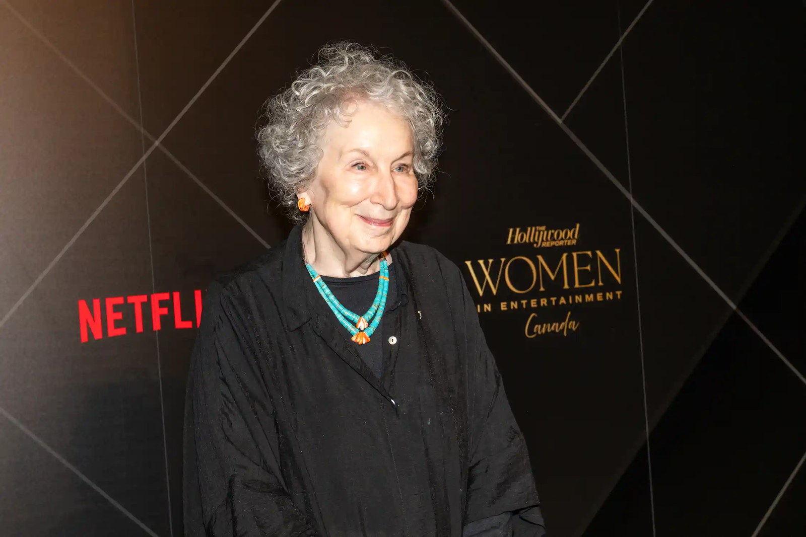 A woman in a dark dress stands in front of a backdrop that says Hollywood and Netflix.