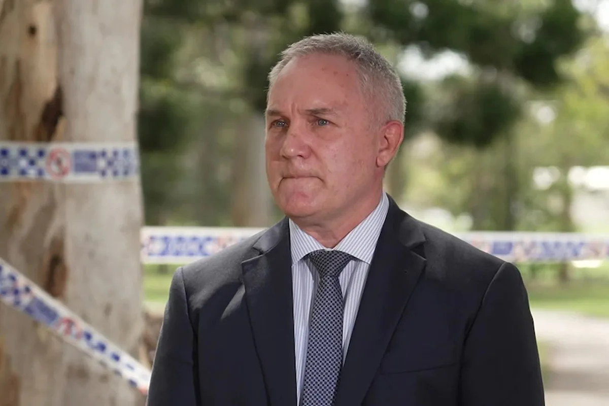 a police detective in a suit and tie stands in front of a tree with police tape