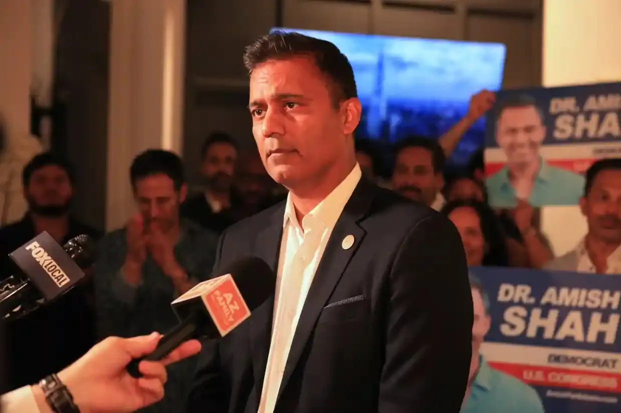 Amish Shah speaks into a microphone while supporters watch behind him