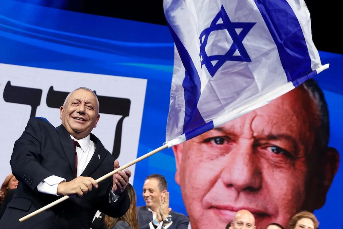 Gadi Eisenkot smiles and waves a flag with a big picture behind him of his own face.