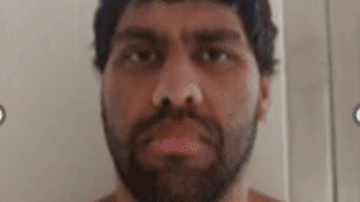 A mugshot-style photo of a dark-haired man with a beard.