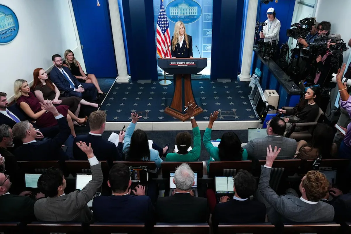 Katie Zacharia speaking with reporters who have their hands up trying to ask questions