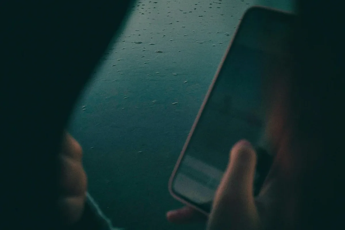 An anonymous male looking at a mobile phone, with a dark background.