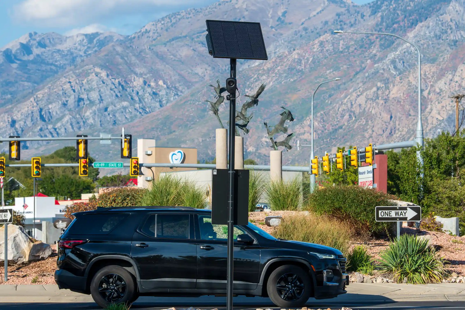 A black car drives by a post with a camera on it.