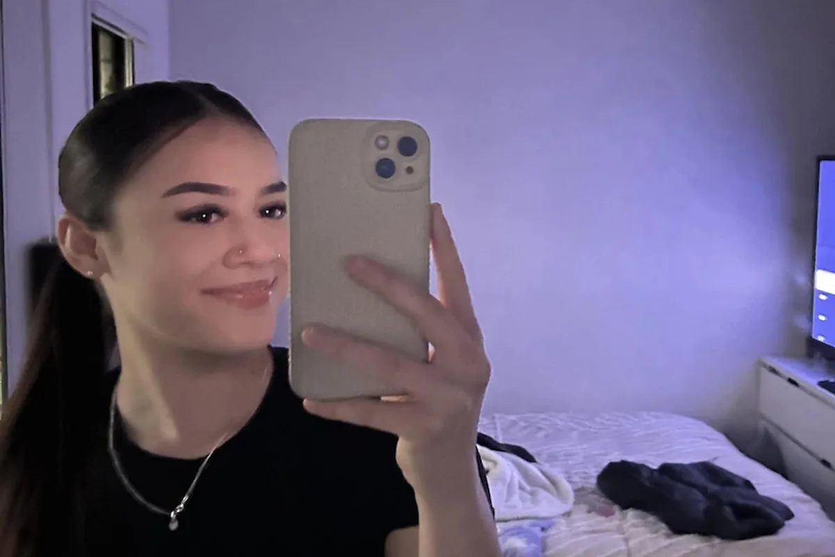 a young teenage girl takes a selfie in a mirror in a bedroom