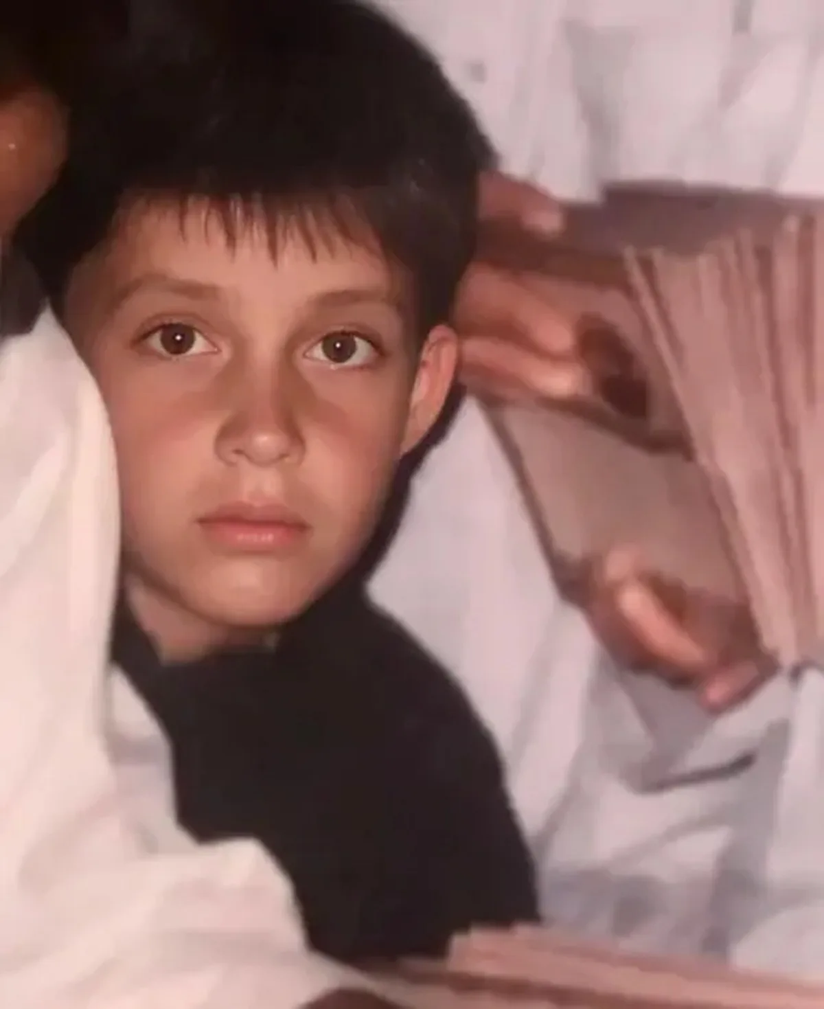A young boy is shown posing for a photo with a serious expression