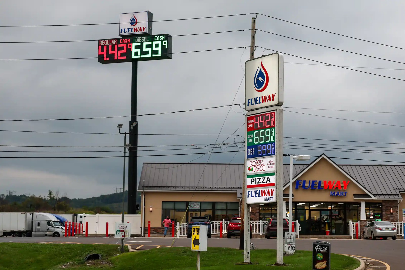 A large sign displays gas prices near a strip mall
