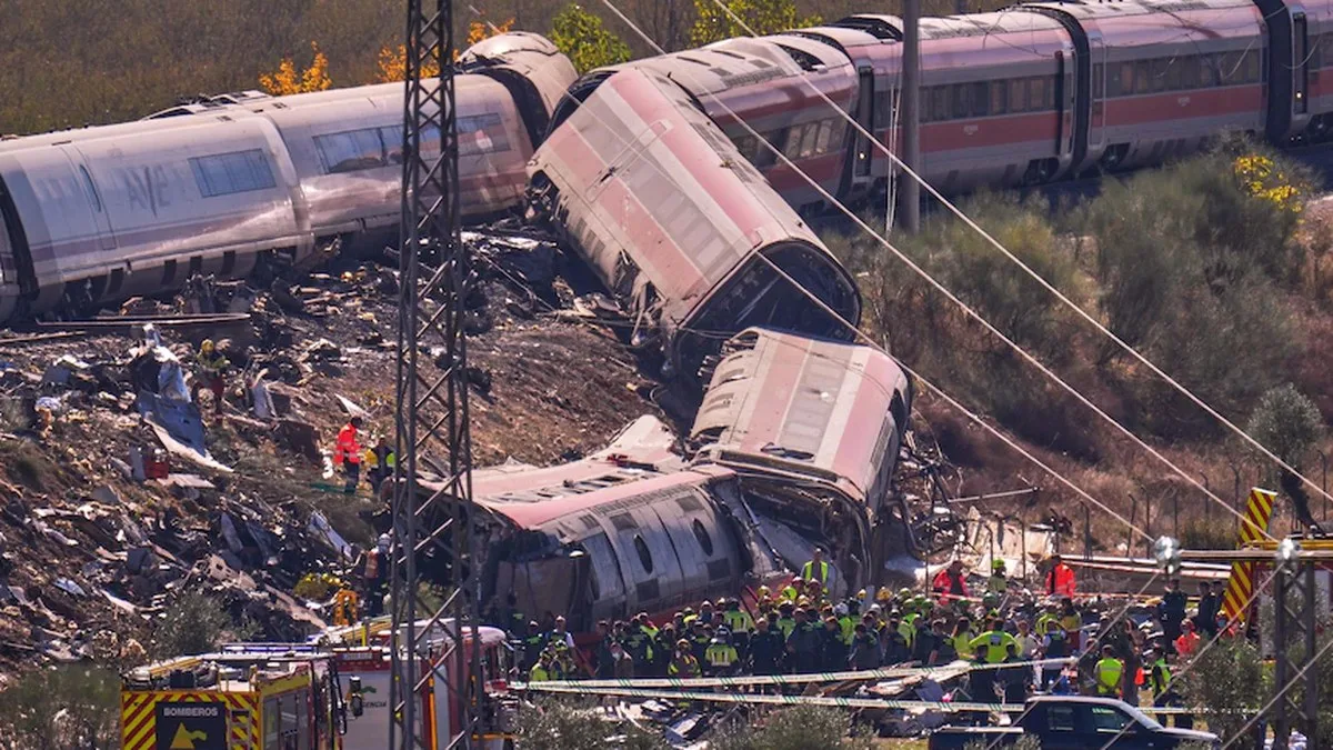 Two derailed trains lying toppled on either side of an embankment surrounded by twisted metal debris and emergency workers.