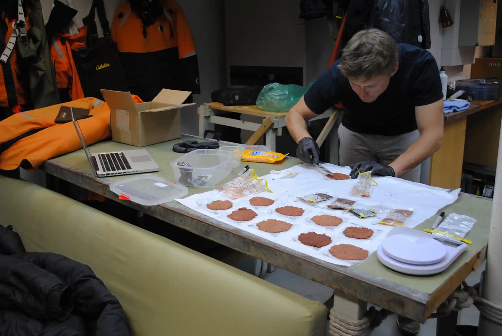 A person bends over a table that holds several small patches of material of varying color.