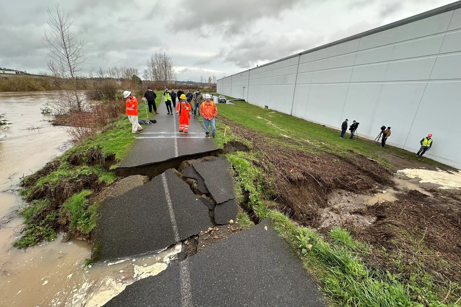 A paved bicycling path atop a levee is broken and slabs of asphalt pavement are tilted into a breach where water poured through.