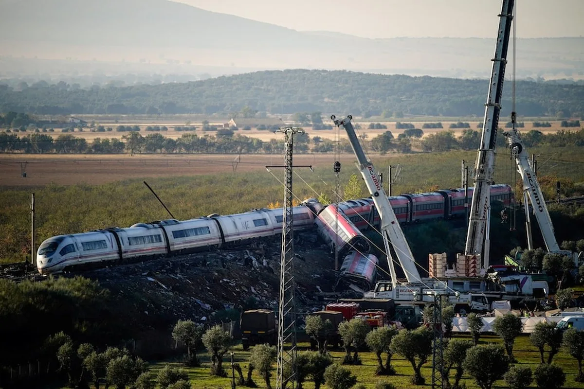 two wrecked trains, rerailed and cranes helping to remove them