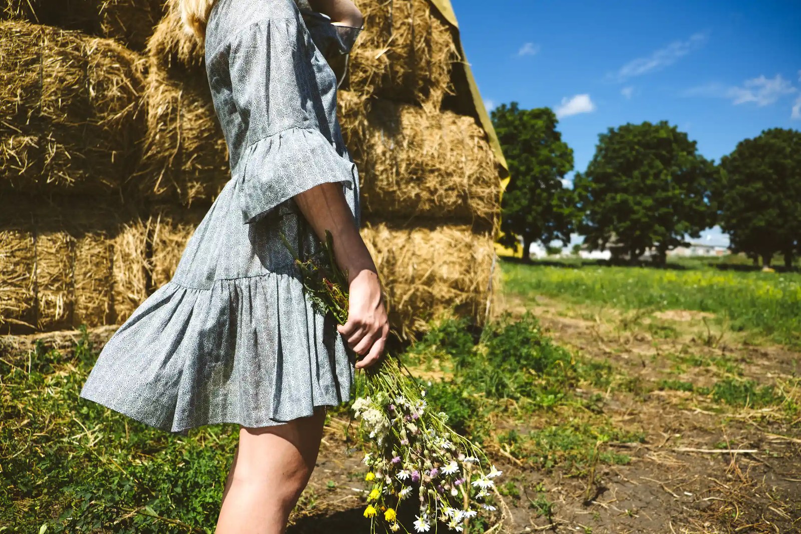 Woman with a bunch of flowers by hay bales.