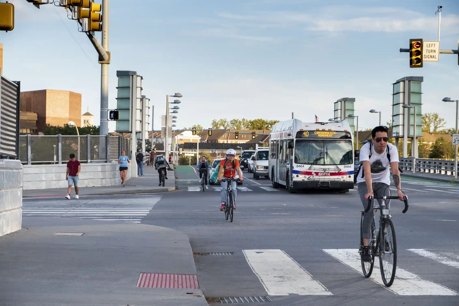 Bicyclists ride down a busy street alongside cars and a bus