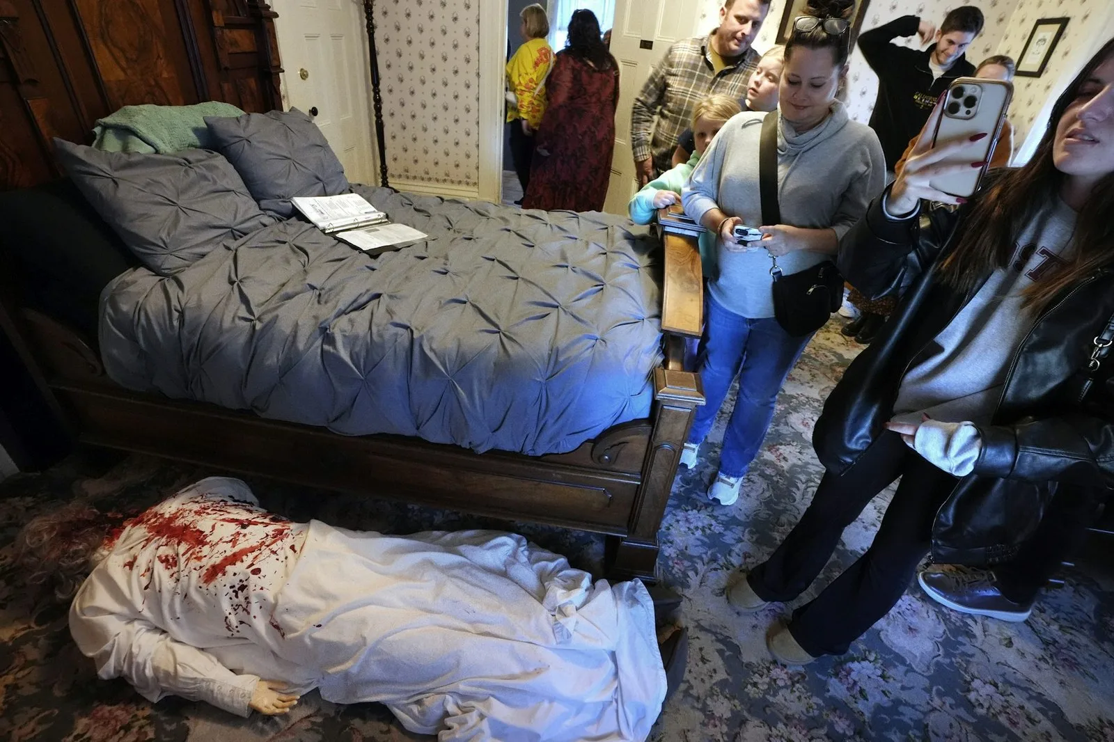 Visitors to the Lizzie Borden House view a mannequin in costume, below left, meant to portray a likeness of the murder scene of Abby Borden, while visiting the site of an 1892 double axe murder, in October 2024, in Fall River, Mass. (AP Photo/Steven Senne)