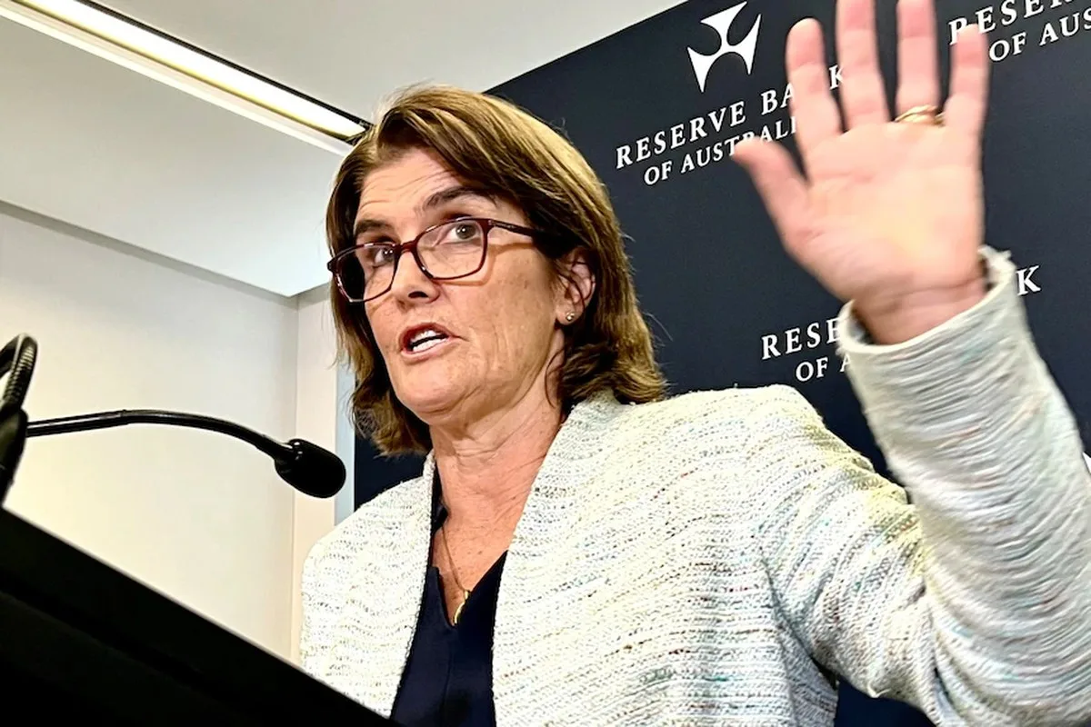 RBA governor Michele Bullock holds her hand up while speaking at a press conference.