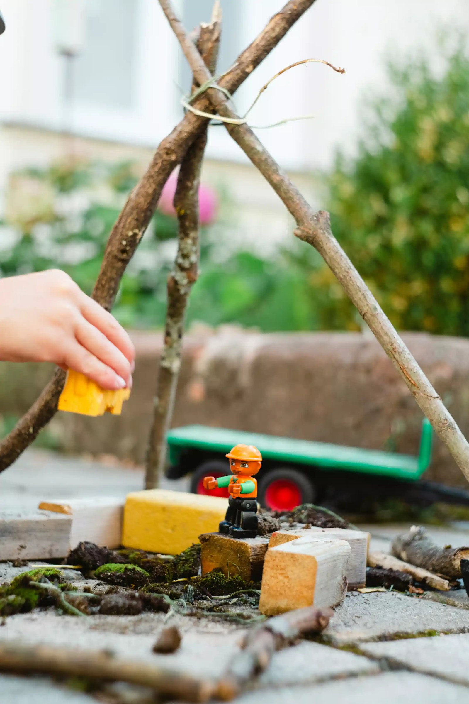 A child's hands playing with blocks and a stick structure outdoors.